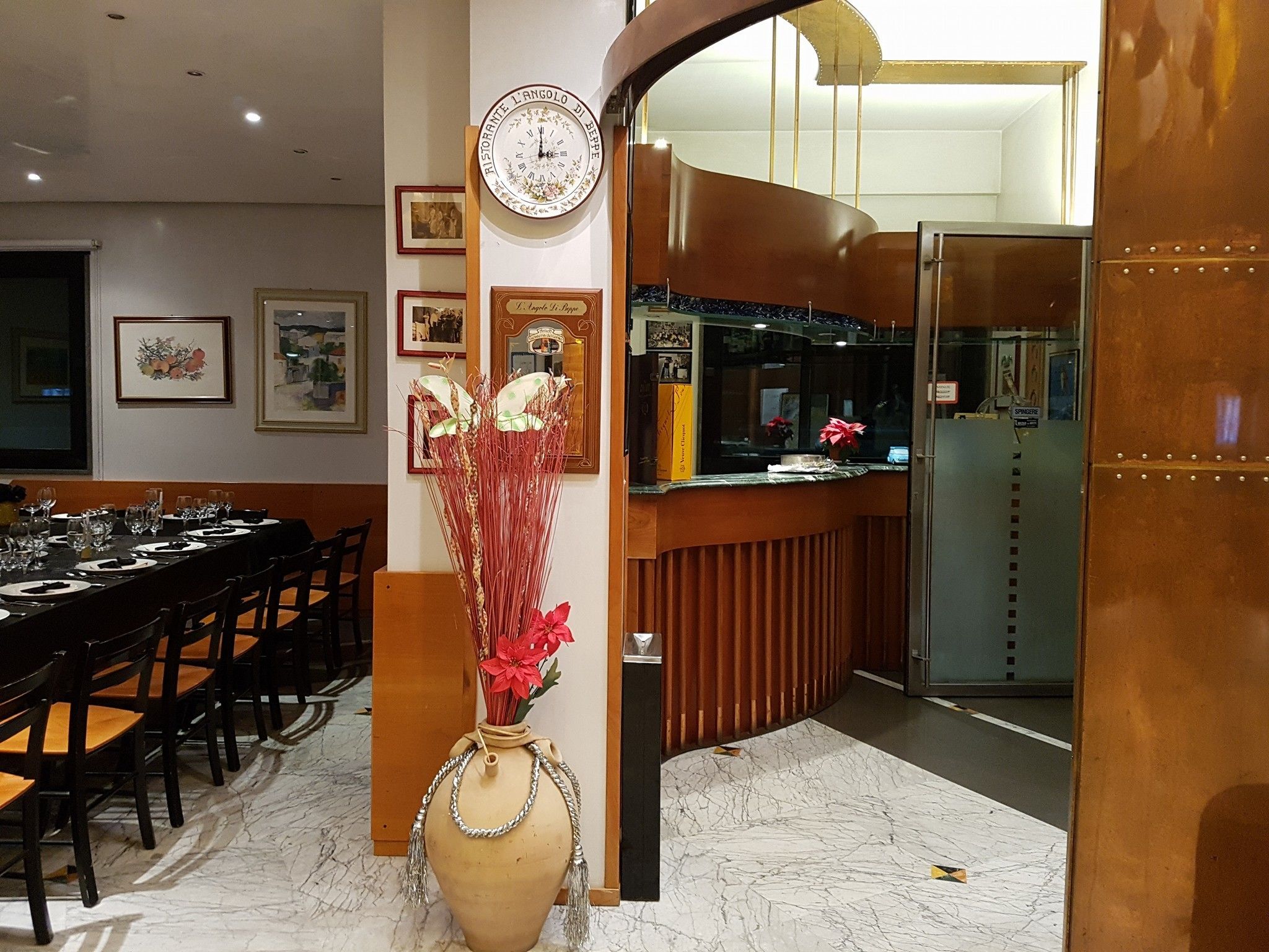 Un coin repas avec une longue table dressée pour le repas, un vase rempli de fleurs rouges et une horloge au mur.