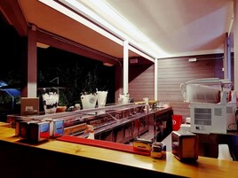 Un área de cocina con una encimera larga, diversos electrodomésticos y un ventanal con vistas a un espacio exterior oscuro.