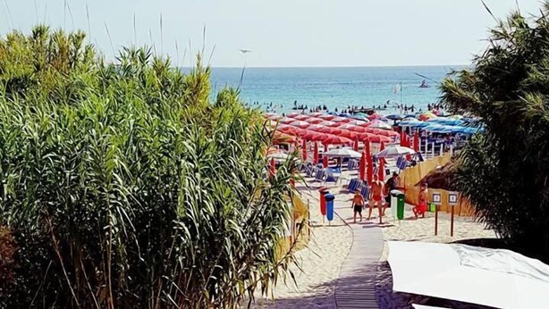 En restaurang vid stranden med uteservering och utsikt över havet, ett trädäck och en gångväg som leder ner till stranden.