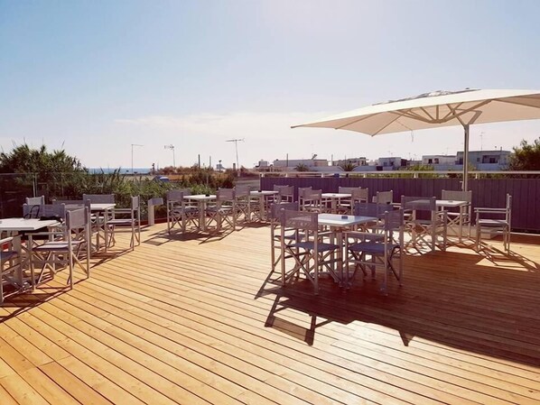 Una terraza de madera con mobiliario exterior y un paraguas grande.
