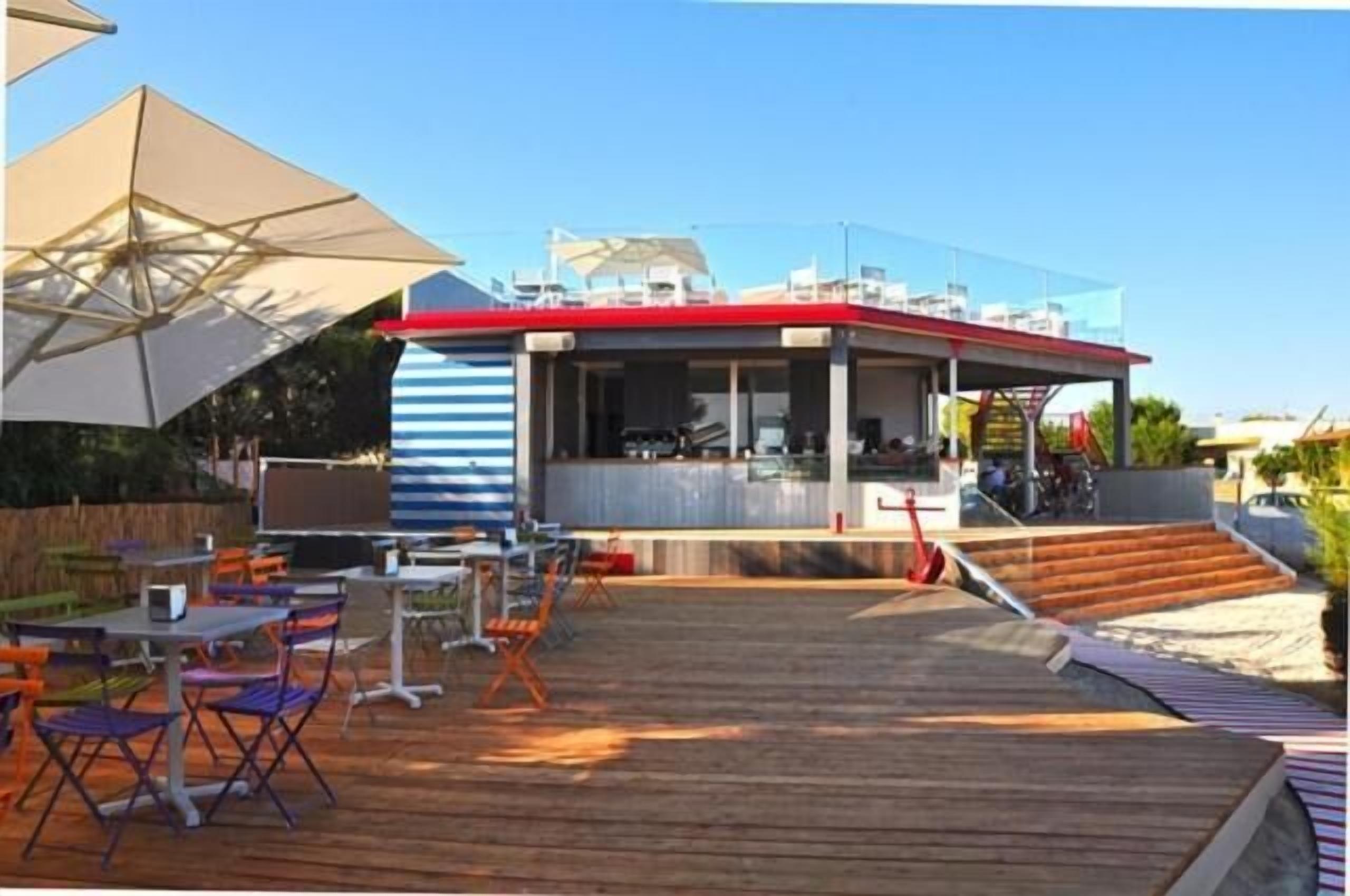Un restaurante con terraza al aire libre en una cubierta de madera, con toldos a rayas y un cielo despejado.