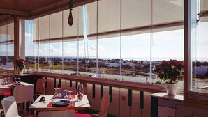 En restaurang med stora fönster som ger utsikt över ett avlägset landskap. Borden är dukade med tallrikar, glas och bestick.