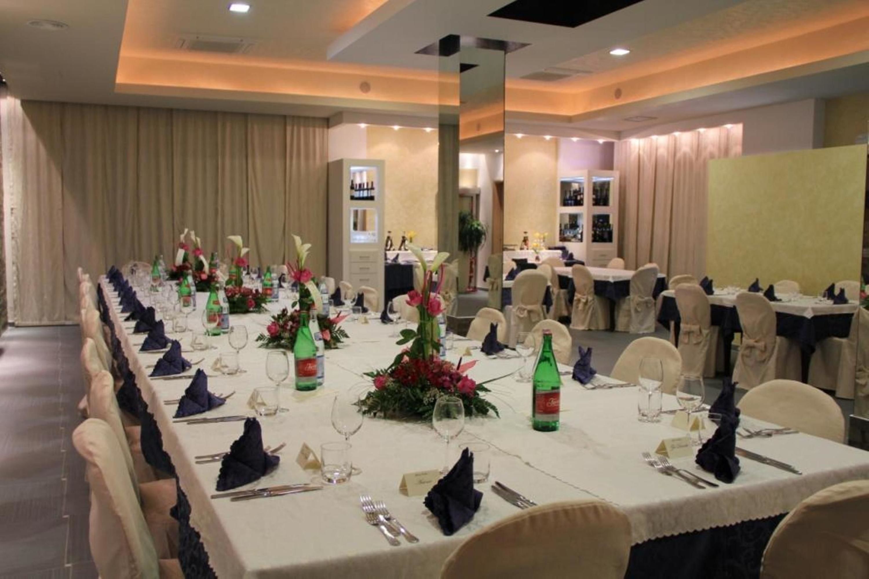 A banquet hall with long tables set for a formal event, featuring floral centerpieces, neatly arranged table settings, and a modern interior design.