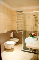 A modern bathroom with two toilets, a shower, and a glass-enclosed vanity.