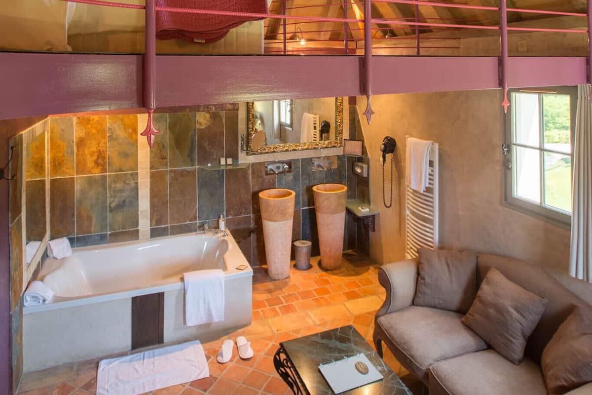 Ein geräumiges Schlafzimmer im Loft-Stil mit großem Fenster, Holzboden und Schlafpritsche, Badewanne und Sofa.