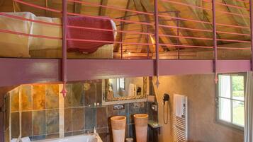 A spacious loft bedroom with a large window, a wooden ceiling, a bunk bed, a bathtub, and a sofa.