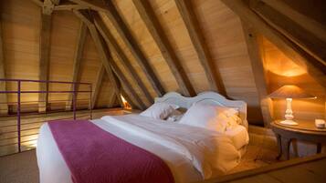 A bedroom with a wooden ceiling, a bed with white linens, a red blanket, and a bedside table with a lamp.