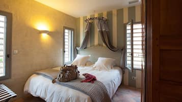 A bedroom with a large bed, a nightstand, a wall-mounted lamp, and a window with curtains.