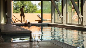 Ein überdachter Swimmingpool mit freiem Blick ins Freie, eine Weinflasche und zwei Gläser am Pool.