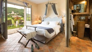 Ein Schlafzimmer mit Bett, einem Fenster mit Vorhängen, einem Nachttisch und Blick auf einen Garten.