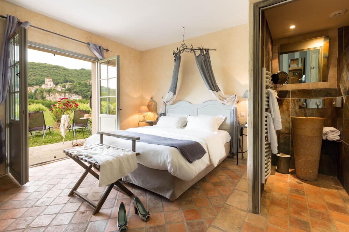 Ein Schlafzimmer mit Bett, einem Fenster mit Vorhängen, einem Nachttisch und Blick auf einen Garten.