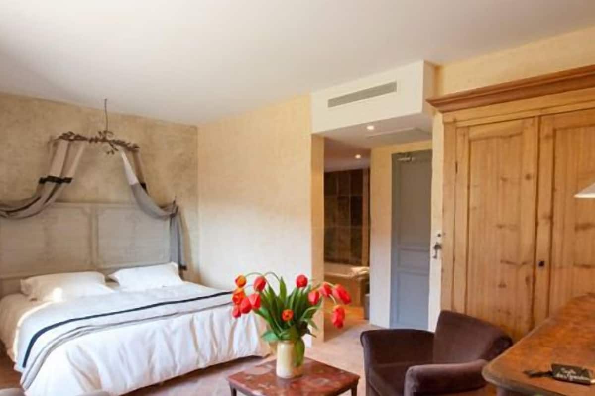 Ein Schlafzimmer mit einem Himmelbett, einem Holzschrank, einem kleinen Tisch mit einer Vase voller roter Tulpen und einem Sessel.