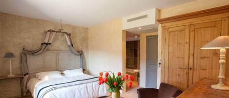 A bedroom with a four-poster bed, a wooden wardrobe, a small table with a vase of red tulips, and a chair.