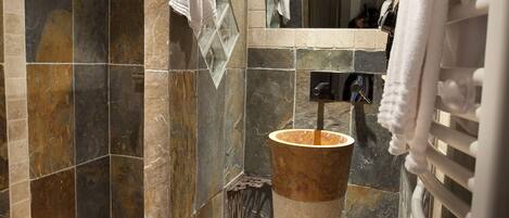Une salle de bain moderne avec une douche en pierre, un grand lavabo et un porte-serviettes.