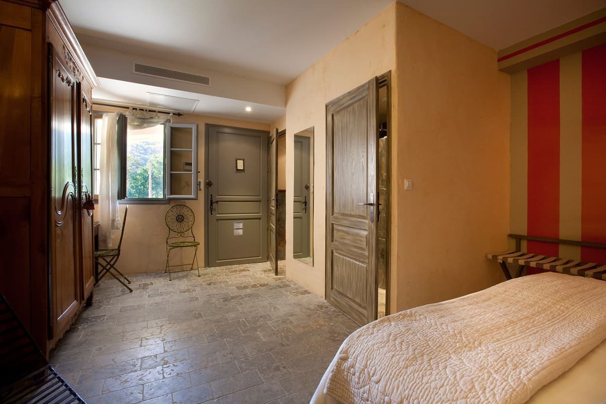Ein Schlafzimmer mit Bett, Sessel, Kleiderschrank und einer Tür zu einem anderen Raum.