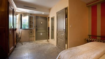 A bedroom with a bed, a chair, a wardrobe, and a door leading to another room.
