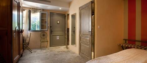 A bedroom with a bed, a chair, a wardrobe, and a door leading to another room.