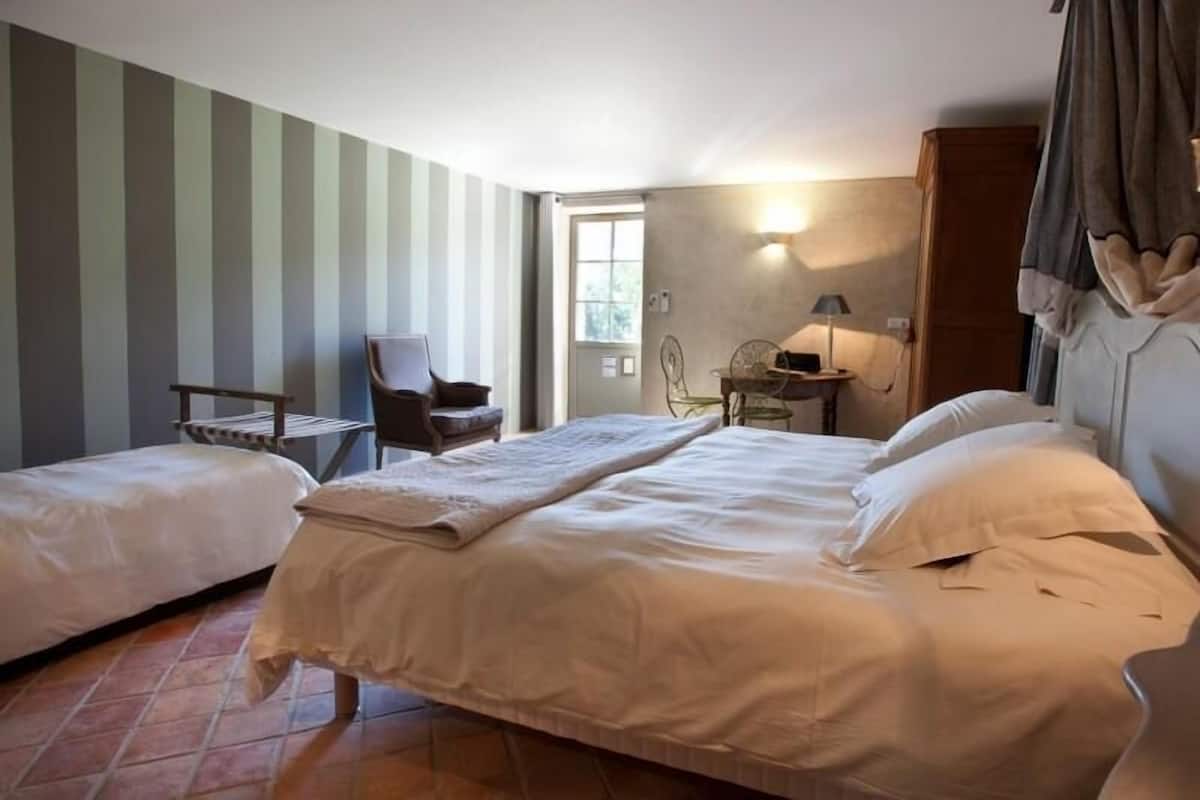 Ein Hotelzimmer mit zwei Betten, einem Sessel, einem Tisch und einer Lampe.