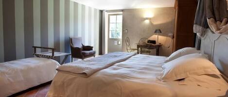A hotel room with two beds, a chair, a table, and a lamp.