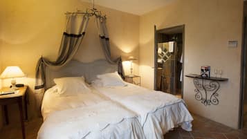 A double bed with a canopy, bedside tables with lamps, a mirror, and a small shelf with glasses.
