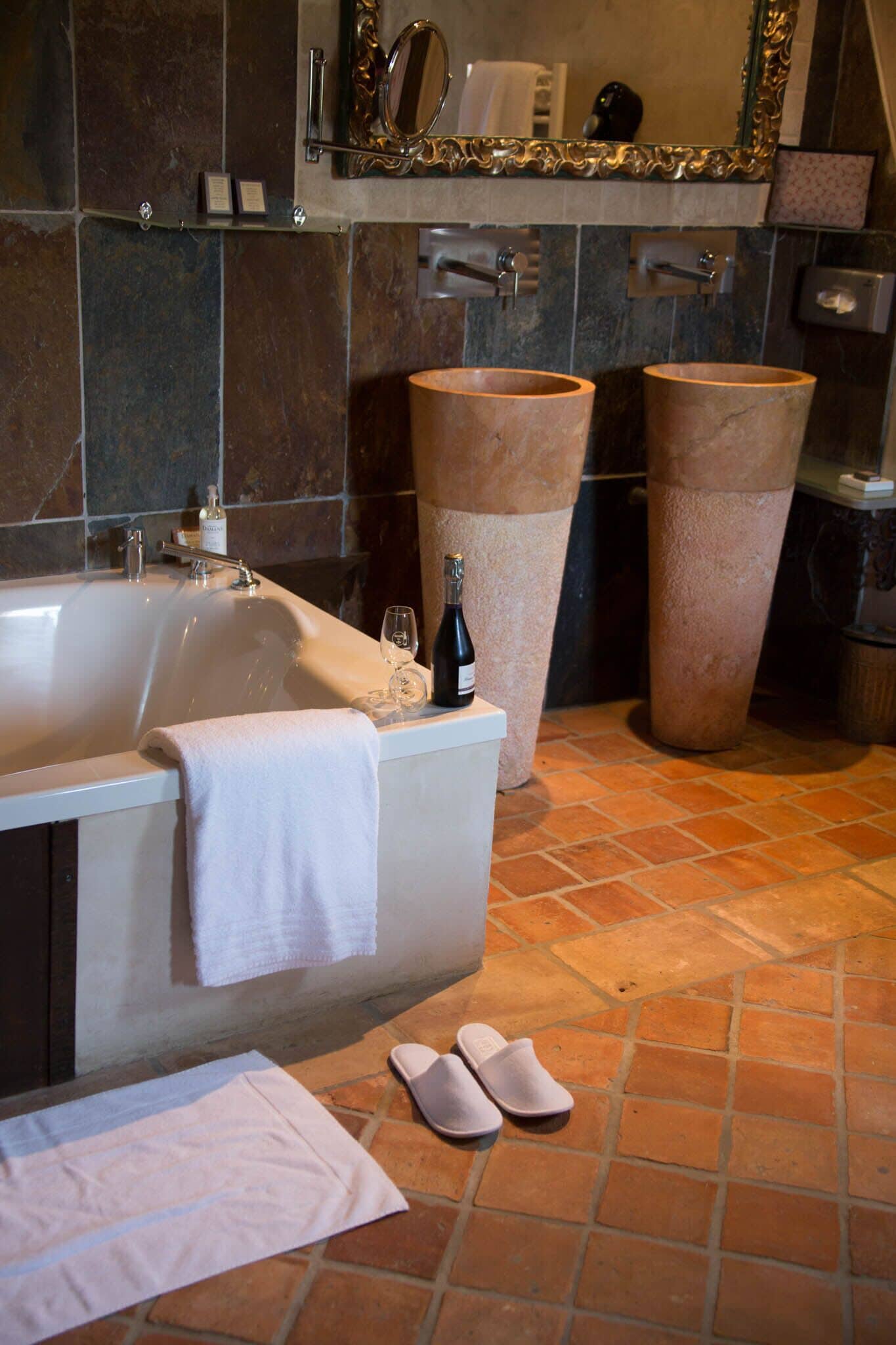 A bathroom with a bathtub, two large stone basins, a mirror, and a towel rack.