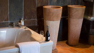 A bathroom with a bathtub, two large stone basins, a mirror, and a towel rack.