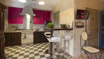 Een keuken met een geruit vloertje, een fornuis, barstoelen en een televisie aan de wand.