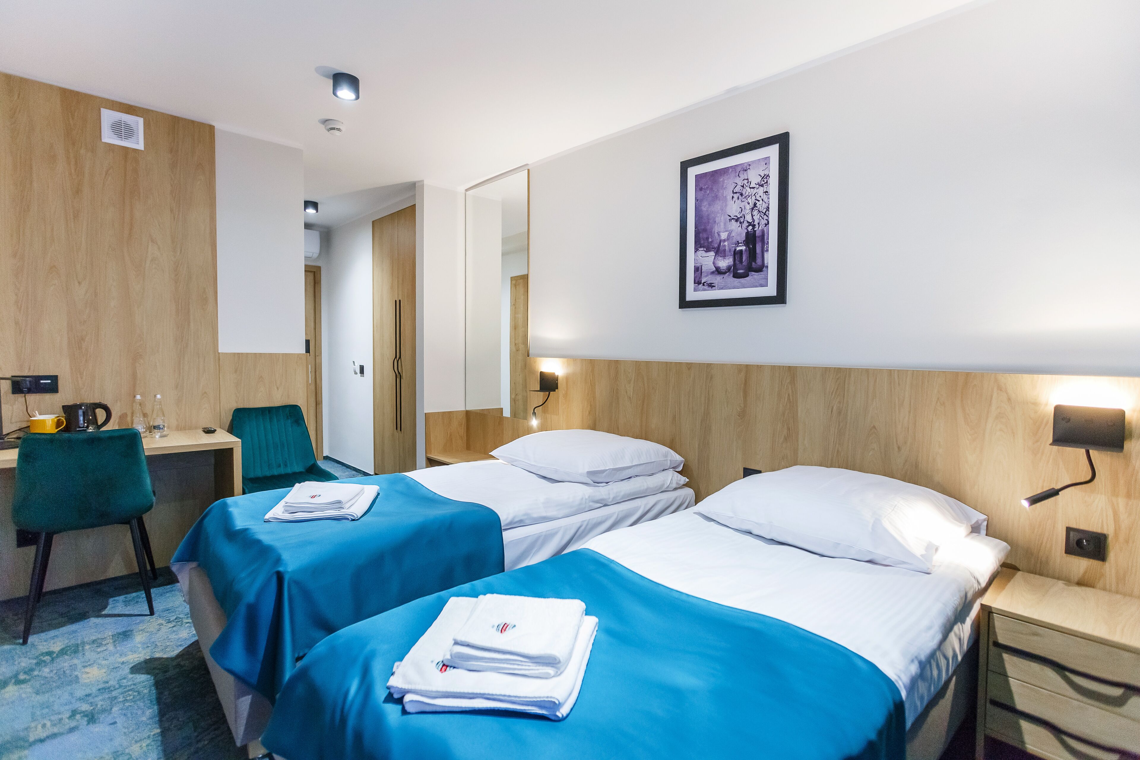 A hotel room with two beds, a desk, a chair, and a framed picture on the wall.