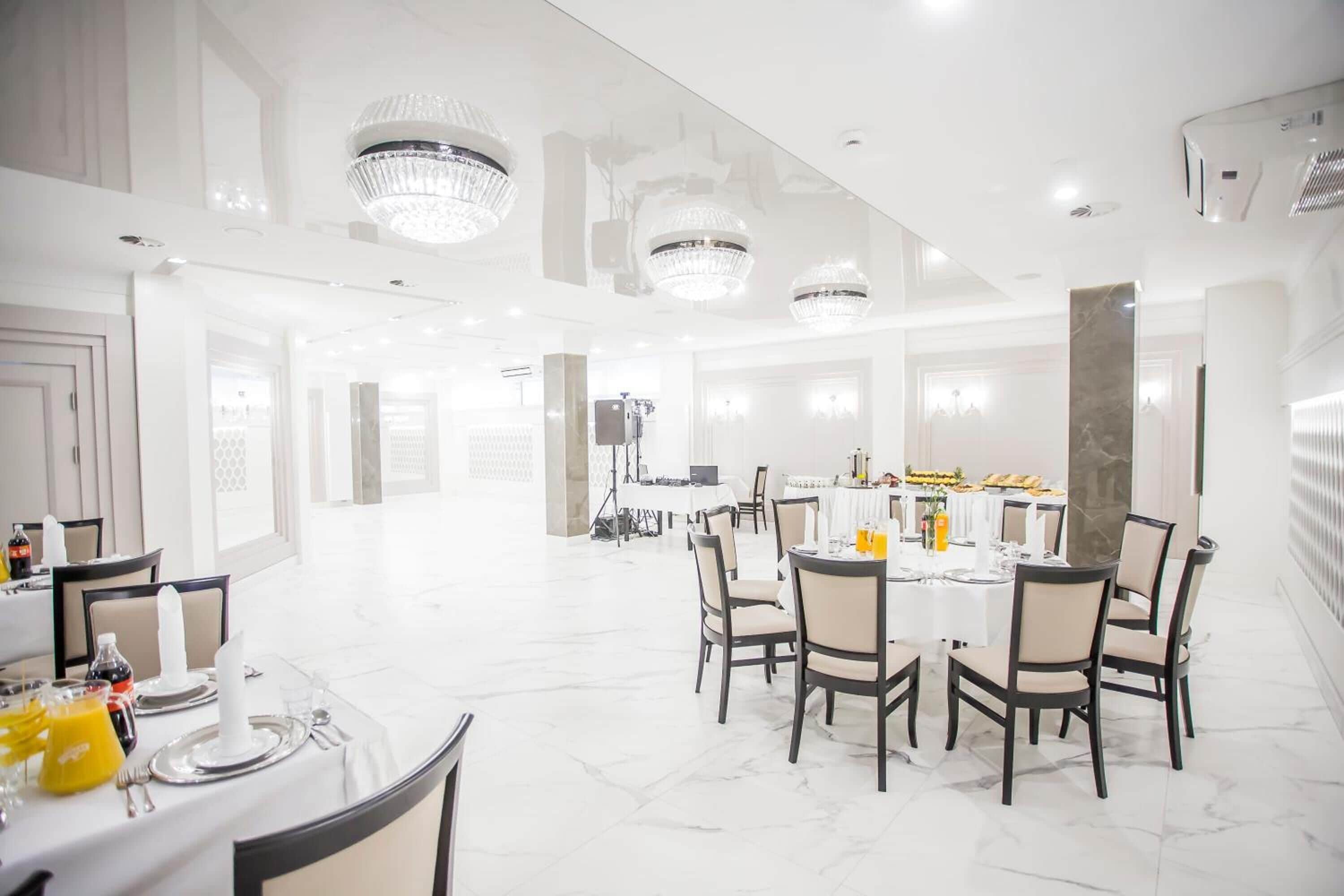Une salle à manger spacieuse et bien éclairée, dotée d’un sol en marbre, d’élégants lustres et d’une table centrale dressée pour le repas.