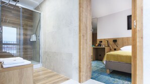 A modern hotel room with a glass shower, a wooden vanity, a bed with a yellow bedspread, and a blue patterned carpet. - Hotel Gromada Lomza (Lomza)