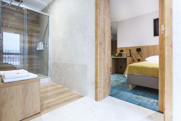 A modern hotel room with a glass shower, a wooden vanity, a bed with a yellow bedspread, and a blue patterned carpet. - Hotel Gromada Lomza (Lomza)
