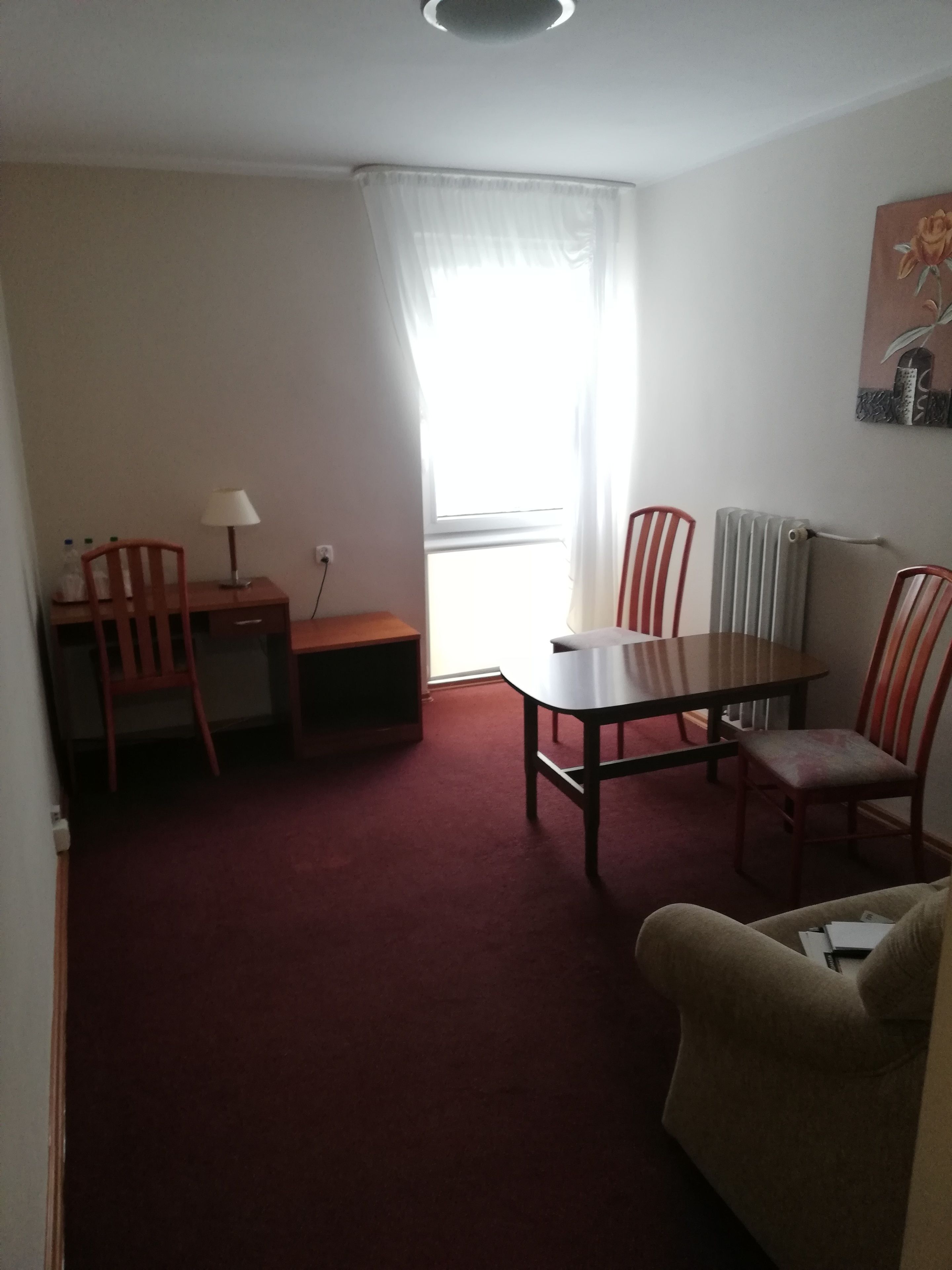 A room with a dining table, chairs, a sofa, a lamp, and a radiator.