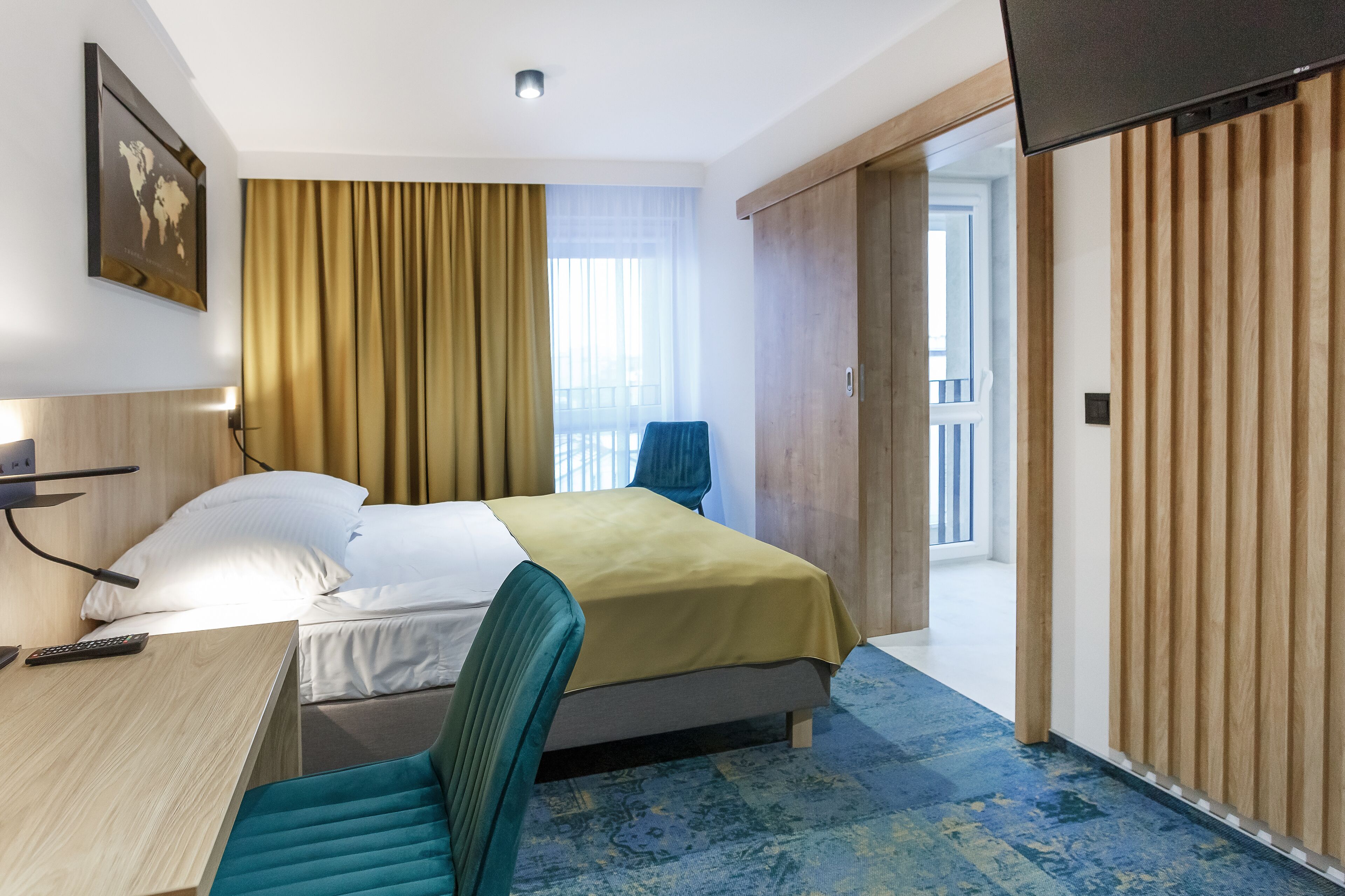 Een hotelkamer met een bed, een bureau met stoel, een televisie en een groot raam met gordijnen.