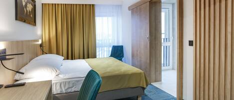 A hotel room with a bed, a desk with a chair, a TV, and a large window with curtains.