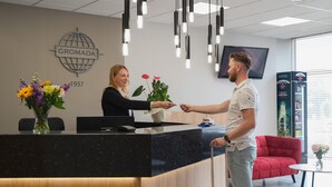 A reception desk with a black countertop, a wooden base, and a vase of flowers. A television is mounted on the wall above the desk. - Hotel Gromada Lomza (Lomza)