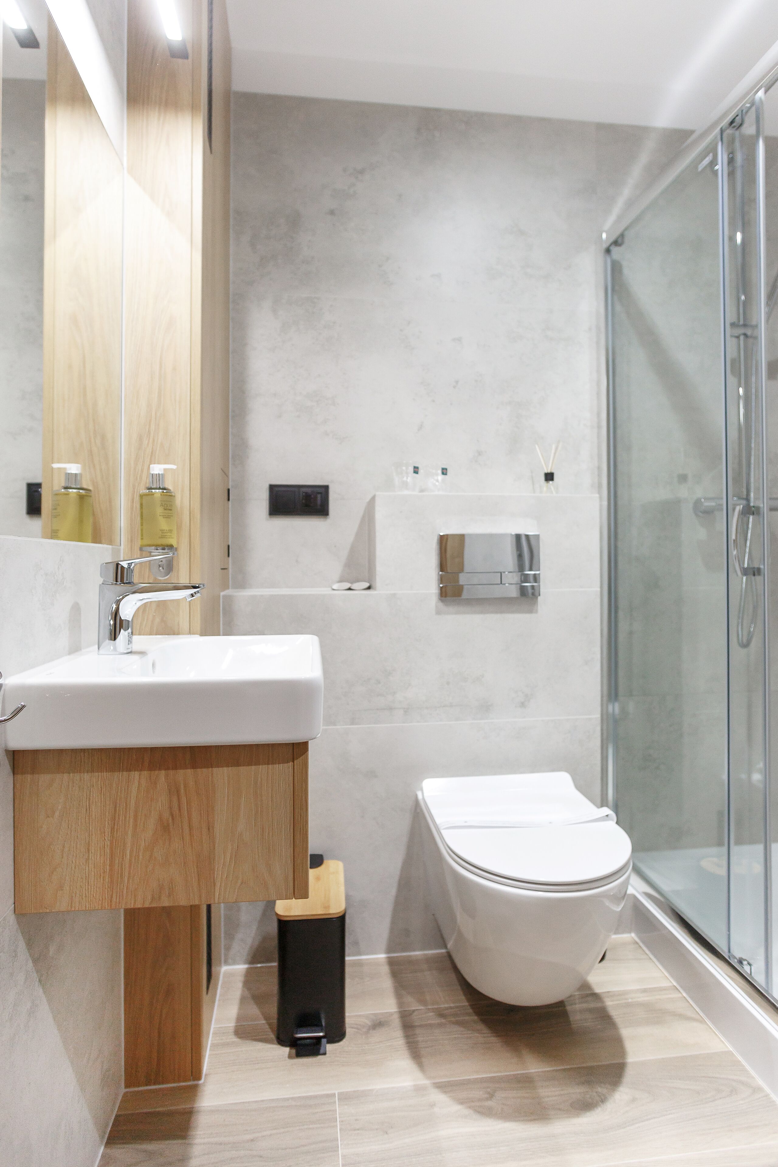 Ein modernes Badezimmer mit einem Holzwaschtisch, einem weißen Waschbecken, einer Toilette und einer Duschkabine aus Glas.