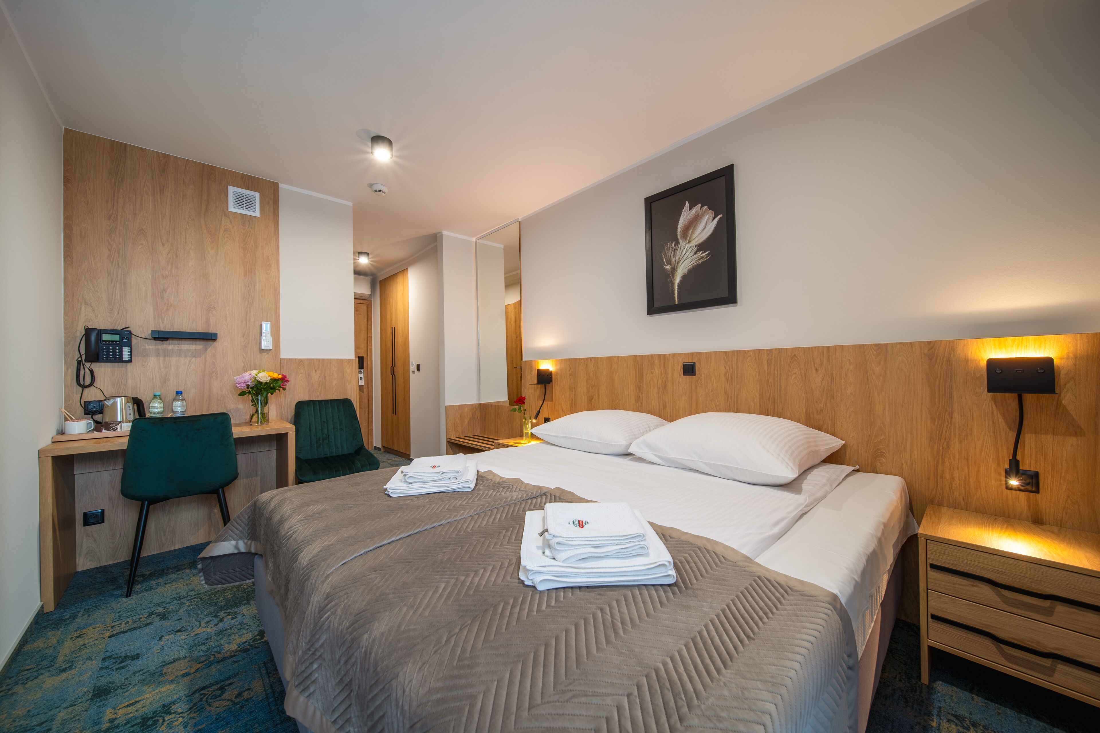 Una habitación de hotel con una cama, un escritorio, una silla, una mesita de noche y una lámpara de pared.