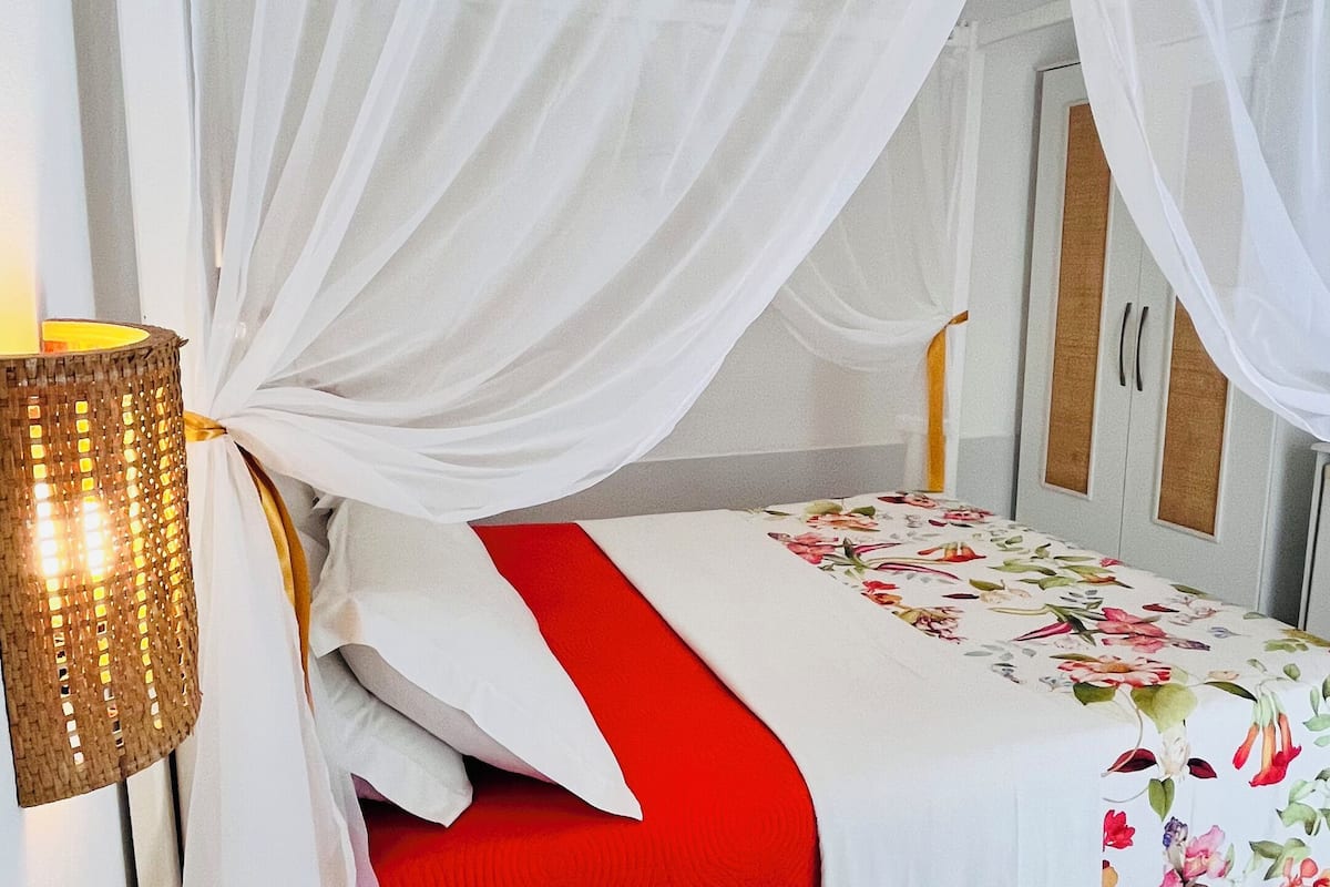 Ein Bett mit weißem Baldachin, einer roten Decke und einer blumigen Tischdecke.