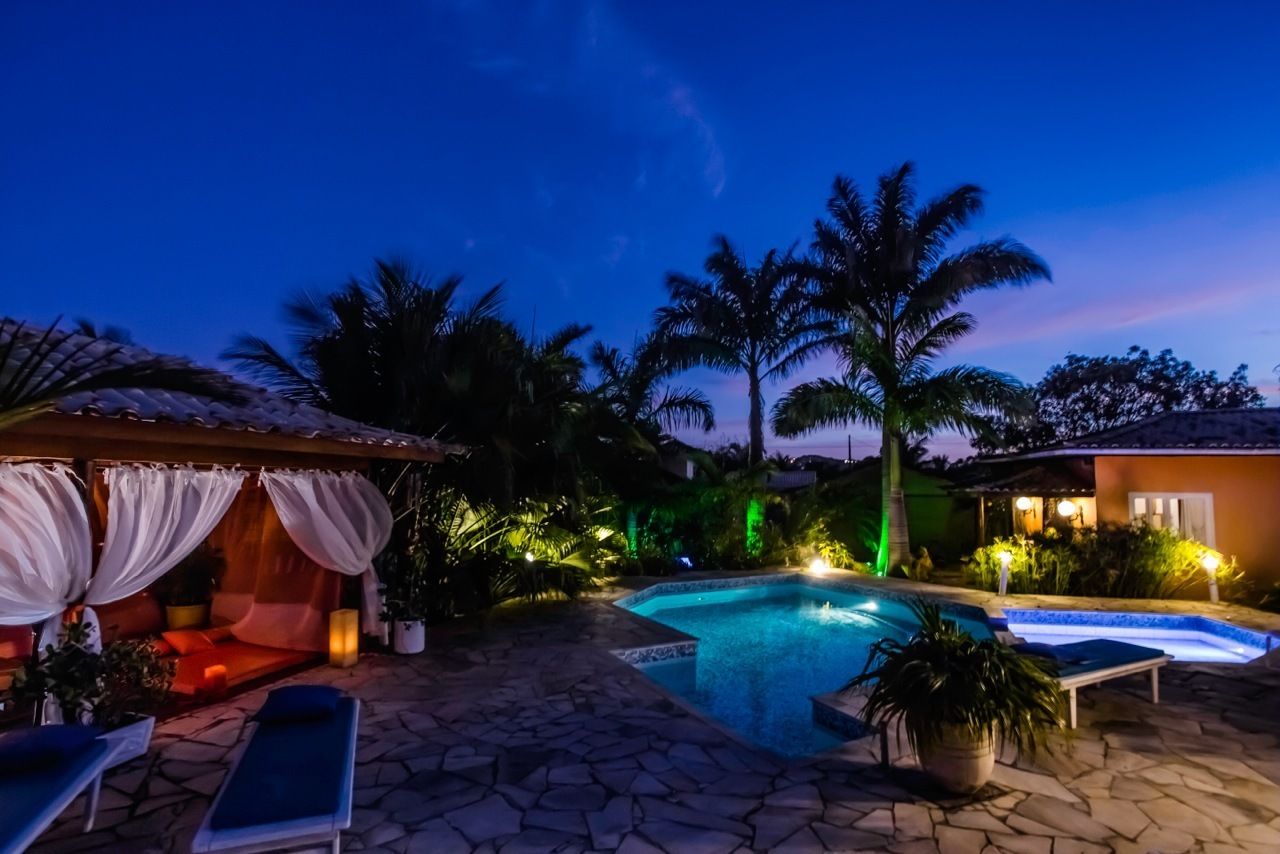 A nighttime pool area with a stone patio, lounge chairs, and a covered seating area with drapes.