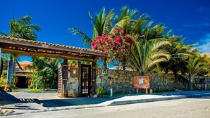 A stone wall with a sign, palm trees, and a building entrance. - Villa Baobá (Búzios)
