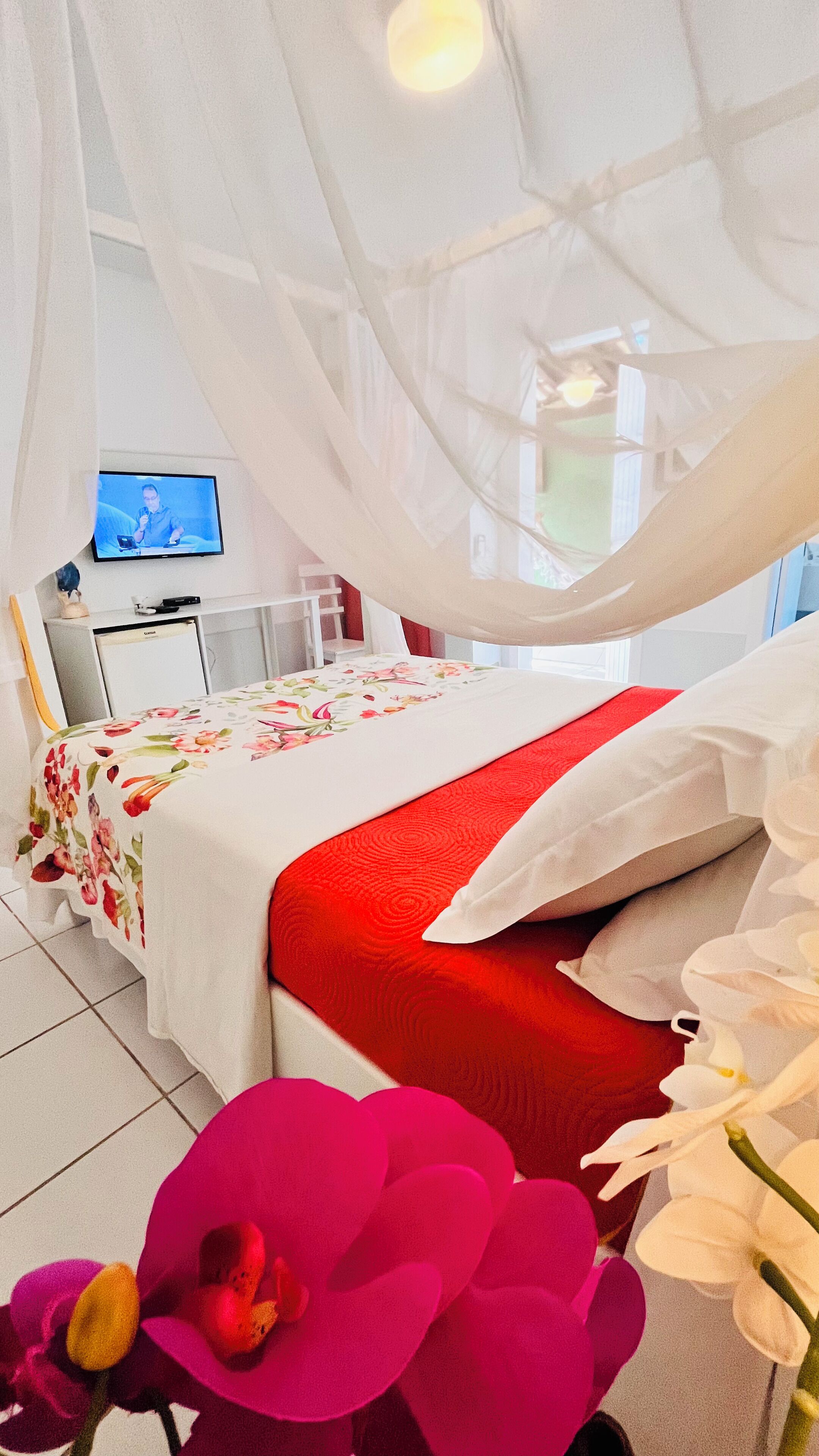 Une chambre à coucher avec un lit sous un dais, un bureau avec un ordinateur et une télévision en arrière-plan.