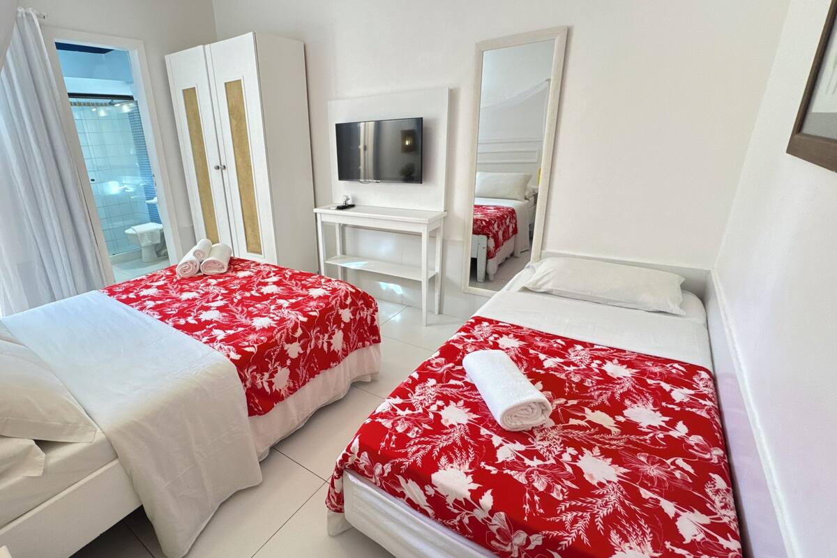 Ein Hotelzimmer mit zwei Betten, einem Fernseher, einem Spiegel und einem Fenster mit Blick nach draußen.