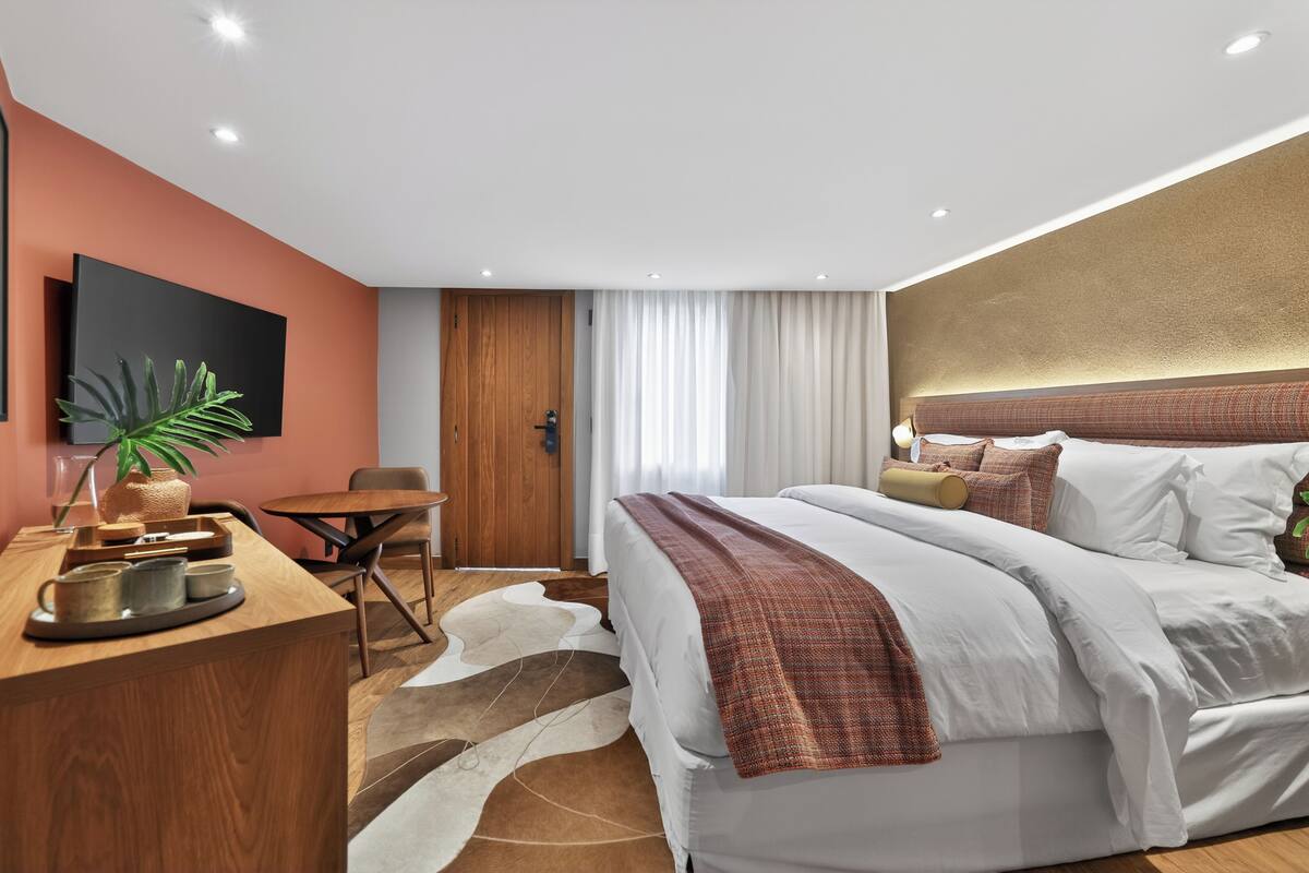 Una habitación de hotel moderna con una cama grande, un escritorio, una silla y un televisor en la pared.