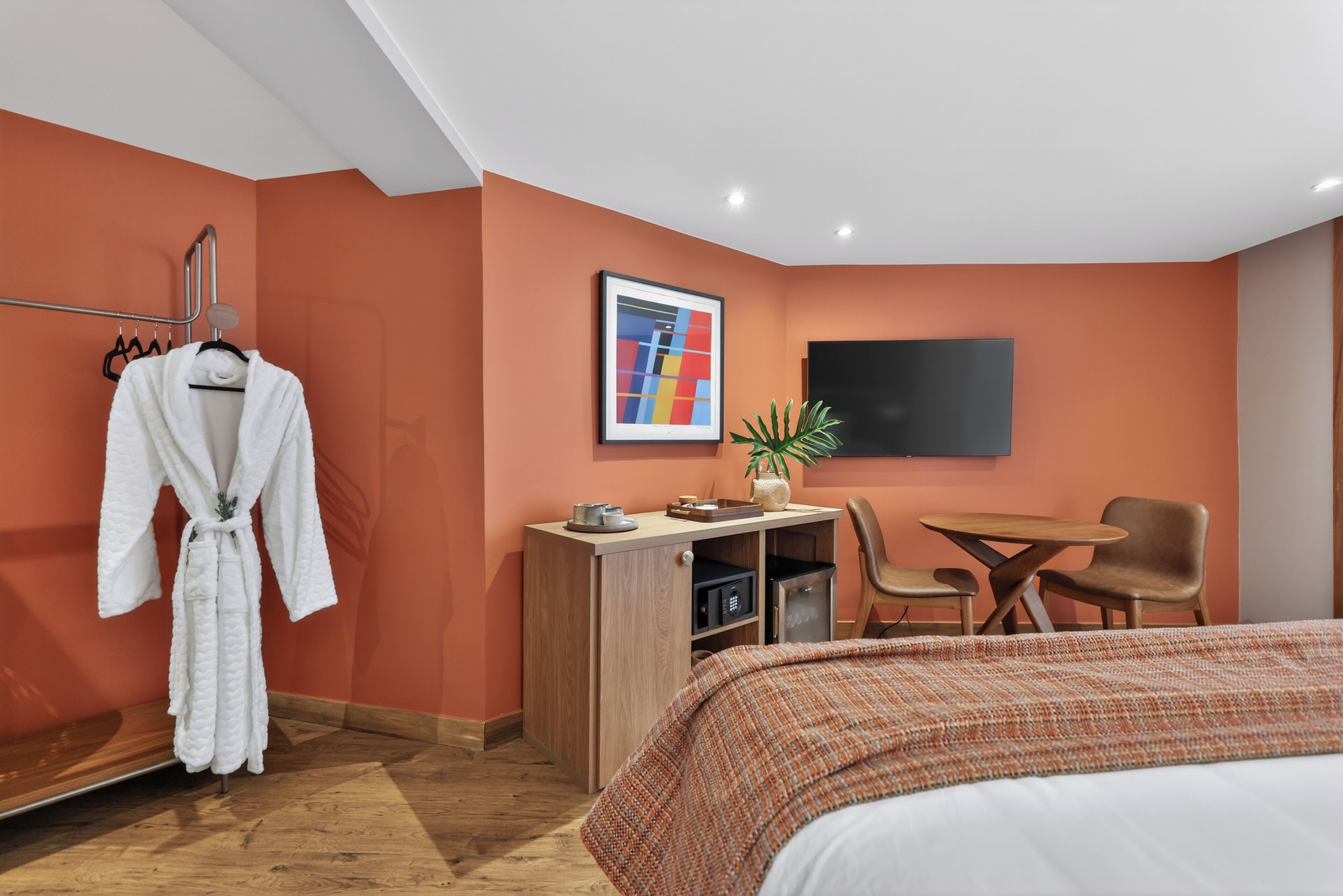 Una habitación de hotel con cama, escritorio, silla, televisión y bata colgada en un perchero.