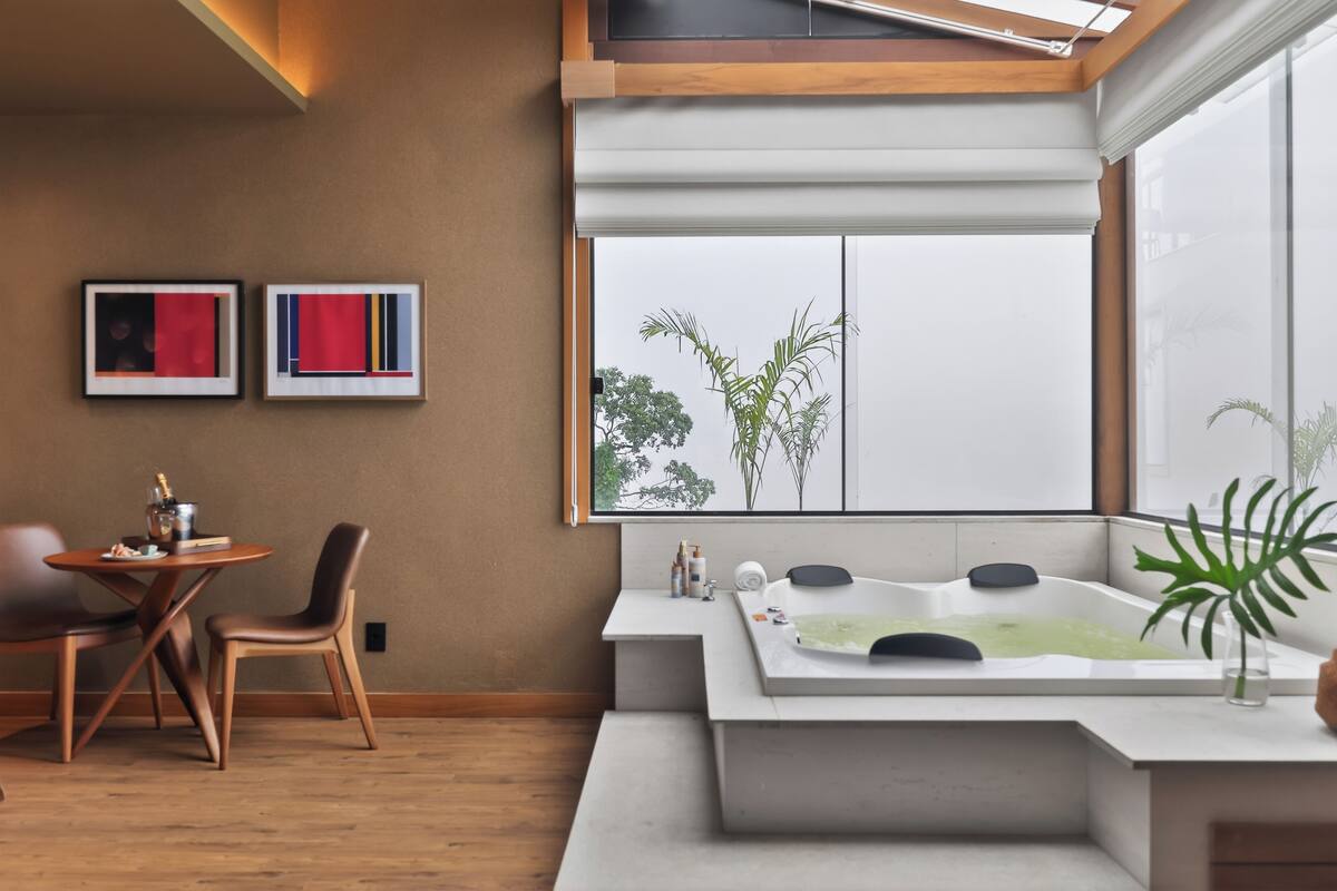 Un baño moderno con un ventanal grande, una bañera y una mesita con artículos de aseo.