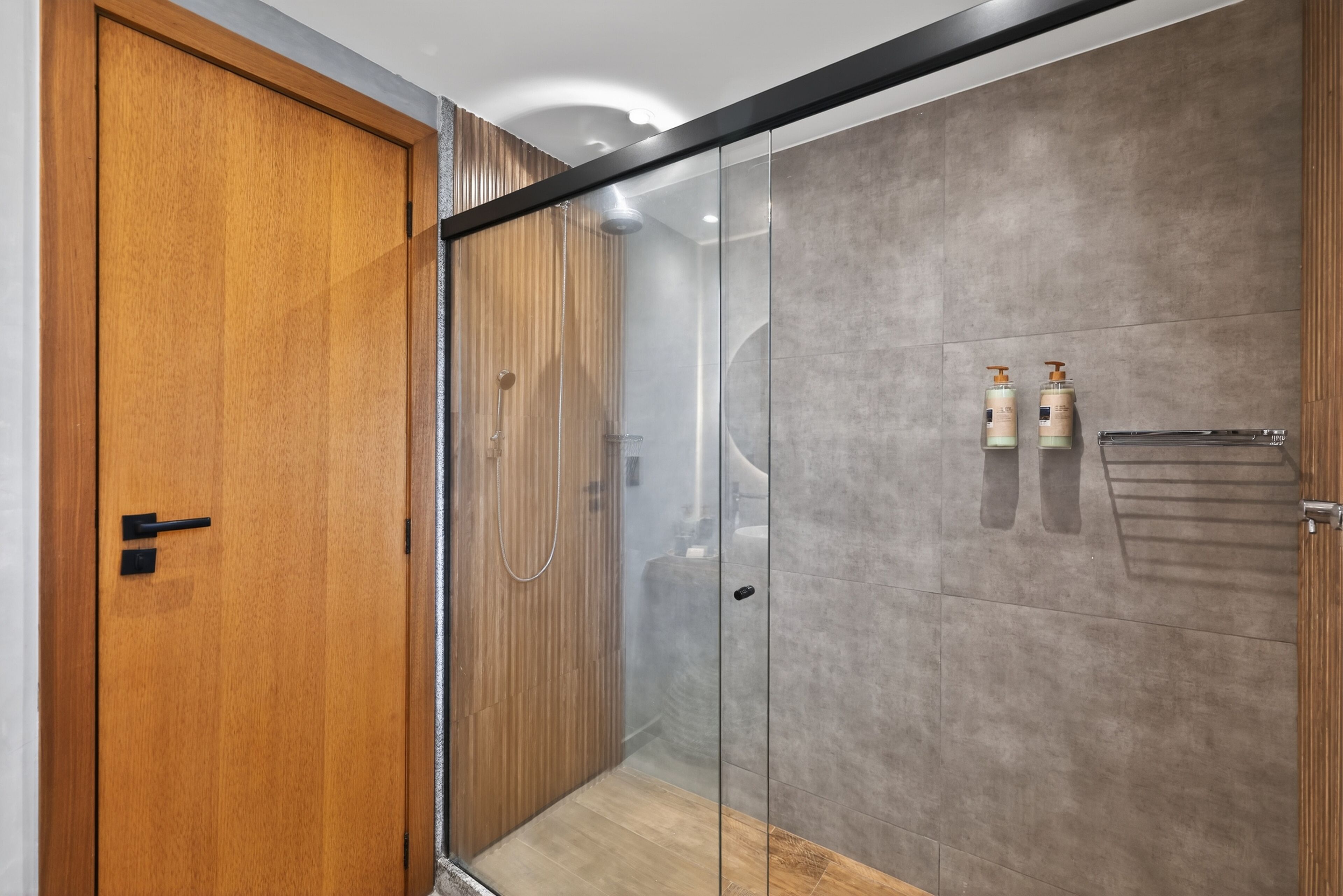 Et moderne badeværelse med en glasbrusekabine, en trædør og to toiletartikler på væggen.