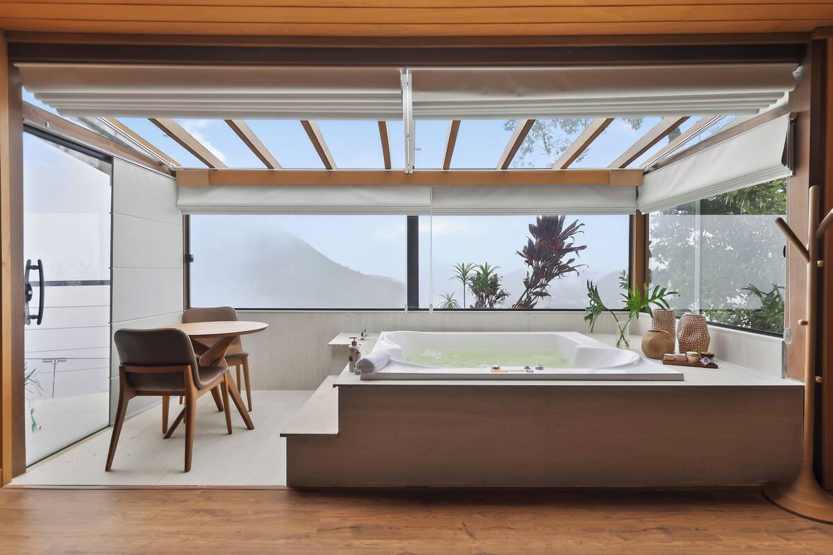 Un baño moderno con una bañera grande, sillas de madera y vistas al exterior.