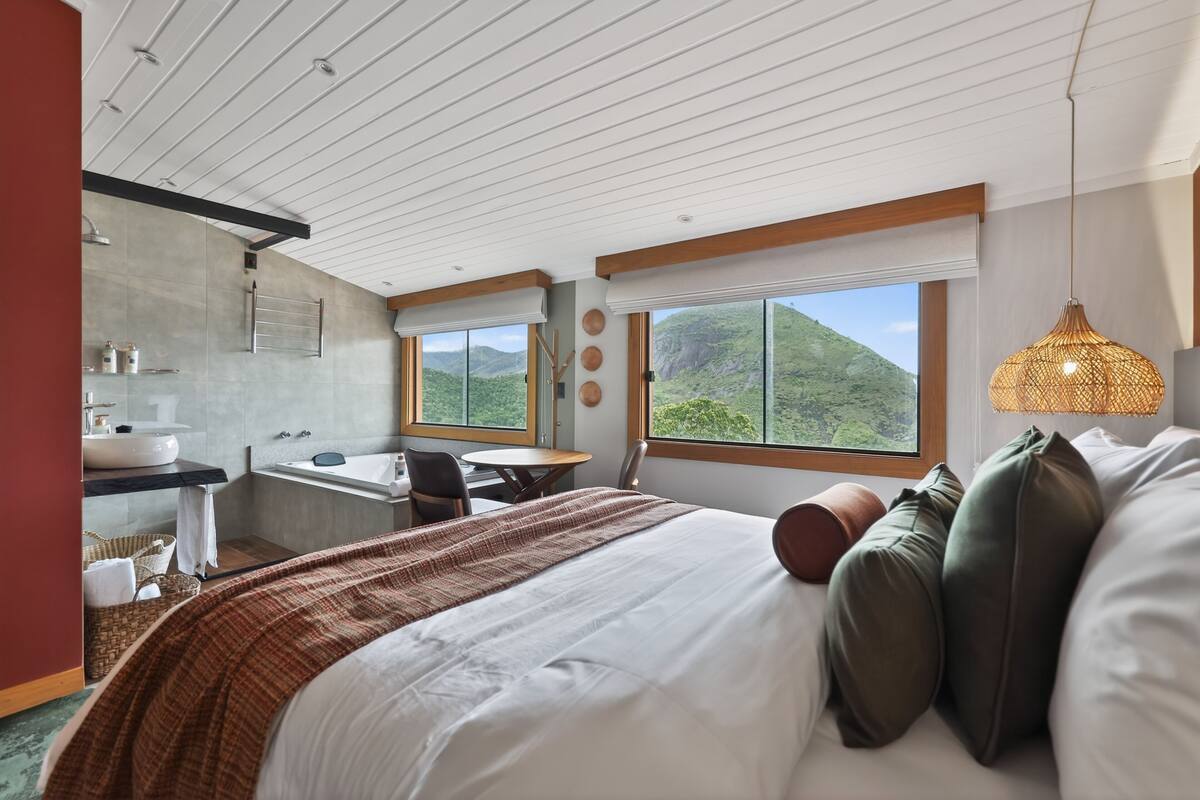 Una habitación de hotel moderna con una cama grande, un escritorio, un baño y vistas a las montañas.