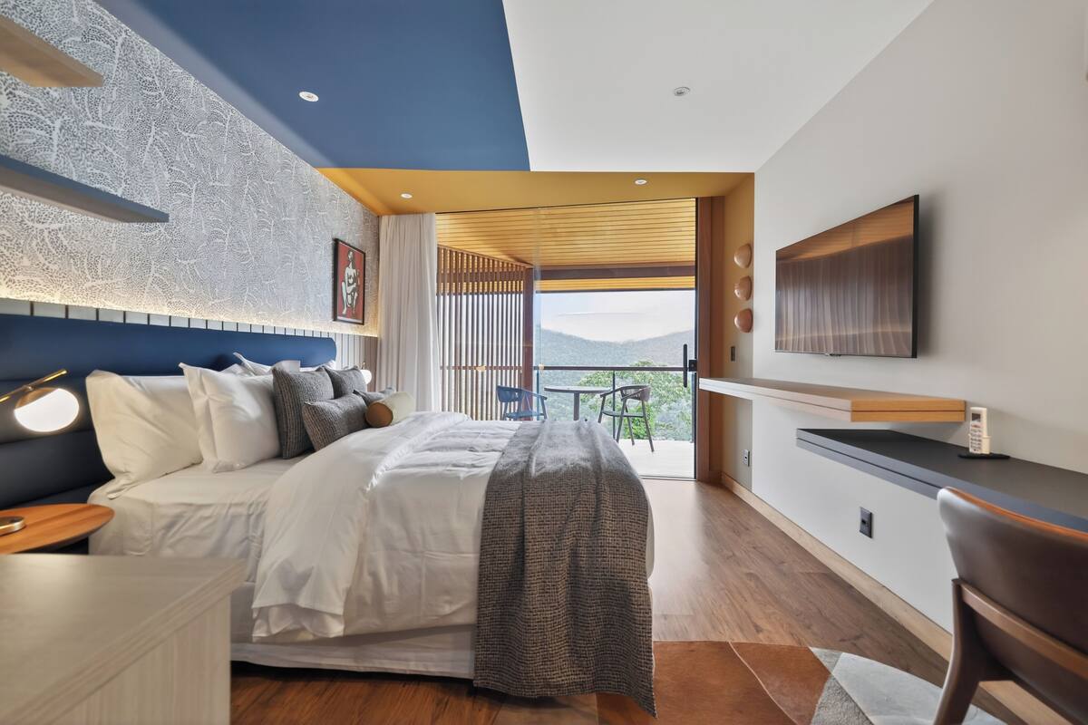 Un dormitorio moderno con una cama grande, televisión, escritorio y balcón con vistas.