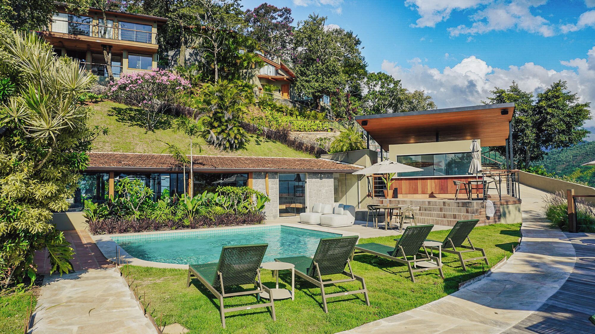 Een modern huis met zwembad, terras en weelderige begroeiing.
